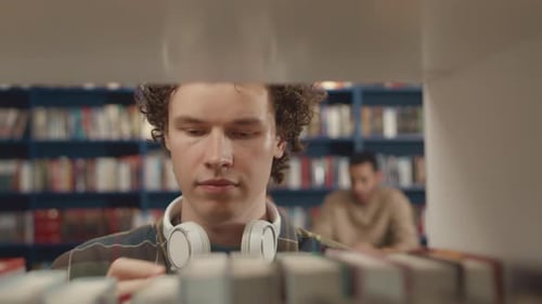 Curly Caucasian Male Student Choosing Book in College Library