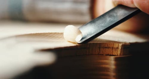 Slow motion macro of master artisan luthier painstaking detailed work on wood violin in a workshop