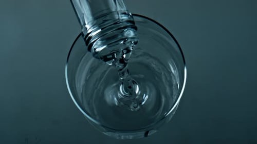 Pure water splashing fills transparent cup in slow motion top view