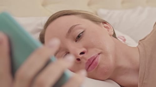 Woman Looks at Her Phone Lying in Bed