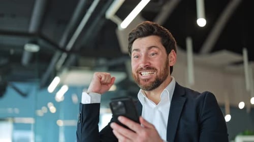 Happy Professional Finds Triumph on Mobile Phone in Modern Office