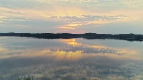 Aerial flight over tranquil lake with reflection on surface of sunlight and clouds at sky