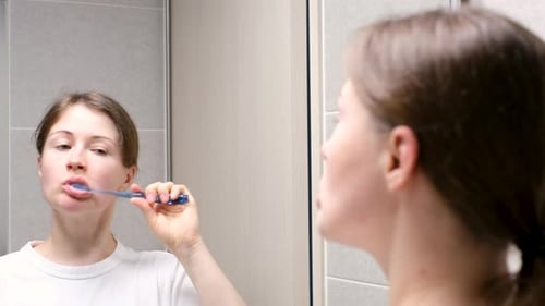 Woman Brushing Teeth in Bathroom Mirror