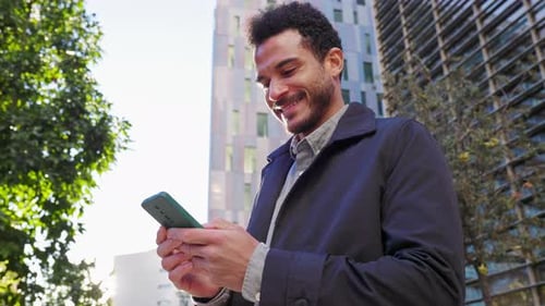 Smiling Young Businessman Using a Smartphone in the City