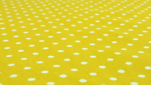 Close-up view of the safety yellow with white polka dots cotton fabric rotated on the display case.