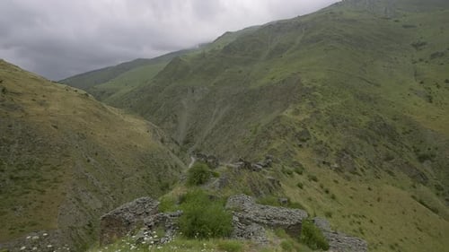 Green mountains with road on cloudy day. Action. Dirt road goes around green mountains with rocks.