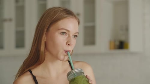 Portrait of Fit Female Drinking Green Juice Detox Cocktail in the Kitchen at Home
