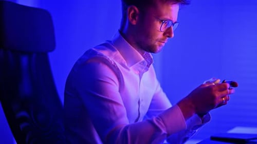 Young Adult Man Using Mobile Phone in Dark Office