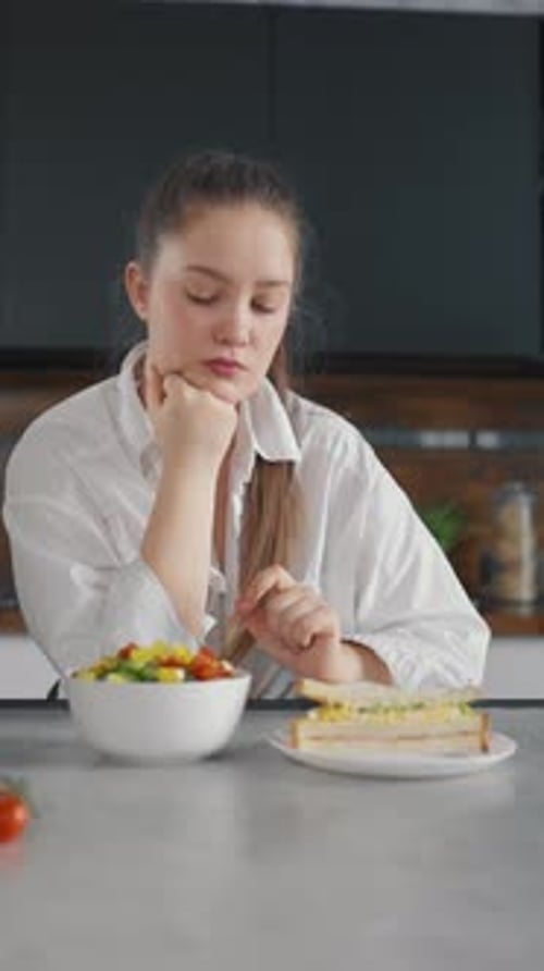 Young Woman Looks At Salad and Sandwich