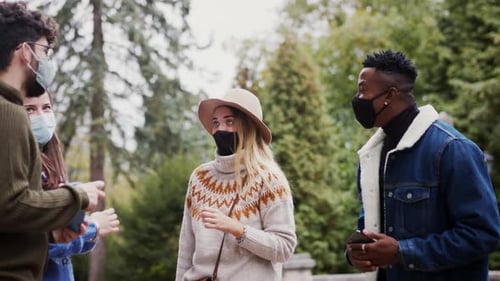 Junge multiethnische Freunde unterhalten sich auf dem Bürgersteig und tragen Gesichtsmasken im Freien