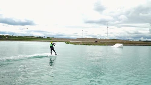 Young man wake boarding in the water park. Man with hydra costume, helmet. Blue water, cloudy day, s