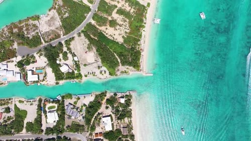 Foward overhead shot of coastal land nestled between canal and beach, revevealing villas and lush