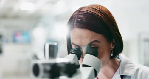 Woman Looks Through Microscope in Bright Lab