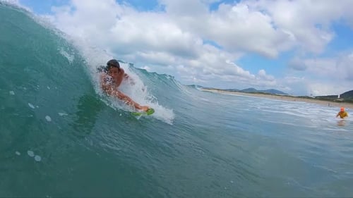 Bodysurfing with handboard, handplane. Young man rides the ocean wave by using his body