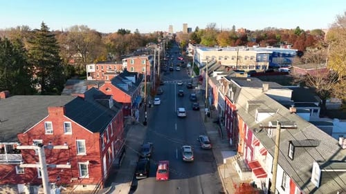 One way street lined with row houses headed towards American city during autumn. Aerial tracking sho