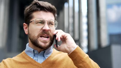Angry dissatisfied businessman arguing talking via phone standing on street near modern office
