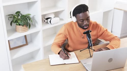 Ouvrant un ordinateur portable, un homme afro-américain prenant des notes, parlant au micro, partageant des idées au bureau à domicile