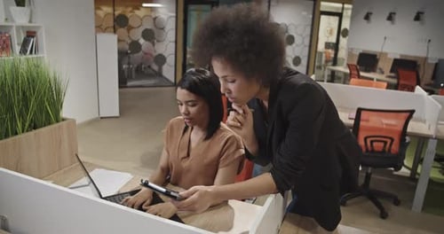 Two Women Collaborating on Laptop and Tablet in Office