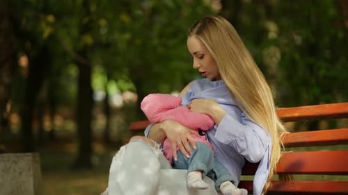 Woman Breastfeeding Child on Park Bench, Daytime