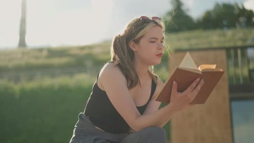 Young Woman Reading Book Outdoors on Sunny Day