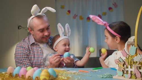 The Family Paints Easter Eggs Sitting at the Table in the Living Room