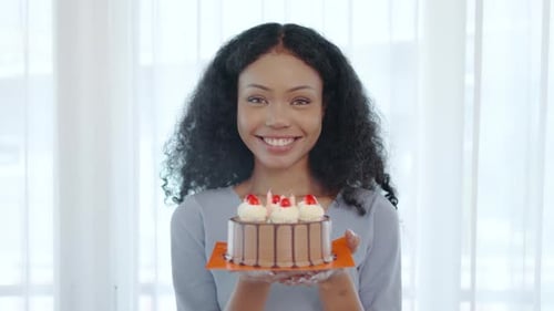 Young asian woman smiles widely as she prepares to blow out the candles on her birthday cake.