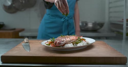 Chef garnishing cooked fish plate in commercial kitchen
