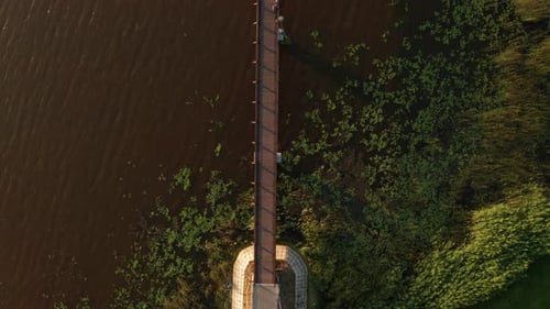 This is an Aerial View of a Wooden Pedestrian Bridge Extending From the Shore Into a Lake Surrounded