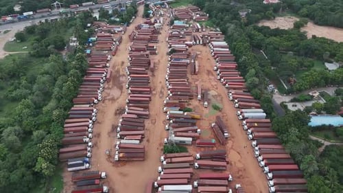 High-angle stock footage of a large, temporary truck depot. Hundreds of reddish semis sit idle,