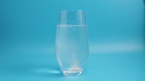 Effervescent tablet in a glass of water close-up on a blue background. Health concept.