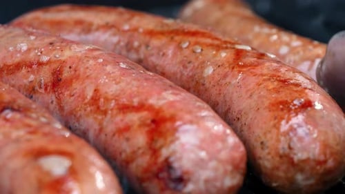 Blick auf Würste, die sich beim Grillen auf dem Grill umdrehen, mit offener Flamme, Nahaufnahme von saftigem Fleisch