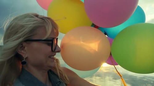 Woman Holding Colorful Balloons on Pier at Sunset