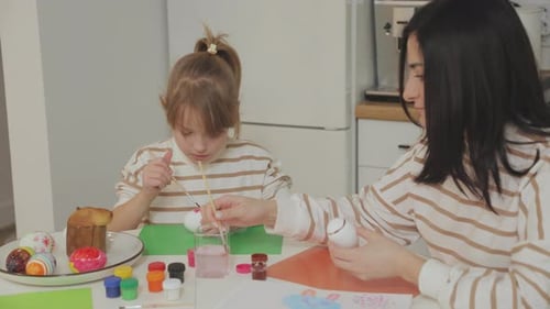 Une jeune belle mère et une charmante fille peignent des œufs de Pâques.