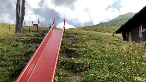 Cute young little girl approaching and sliding down a slide in slow motion with mountains in the bac