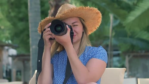Photography and Travel A Young Woman in a Hat Holds a Camera and Takes Pictures on the Beach