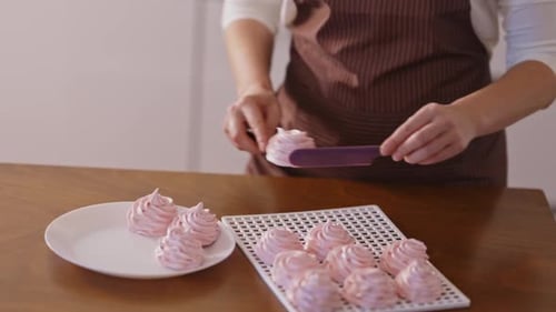 Woman Transfers Pink Meringues from Rack to Plate