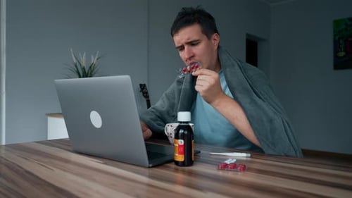 Sick Man Reads Pills Instruction While Working on Laptop