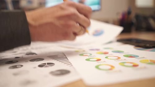 Hands Analyzing Financial Data with Pencil in Office