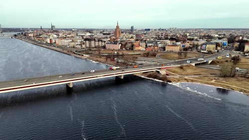 Aerial of highway bridge spanning a wide, blue river Daugava in a densely populated city Riga with t