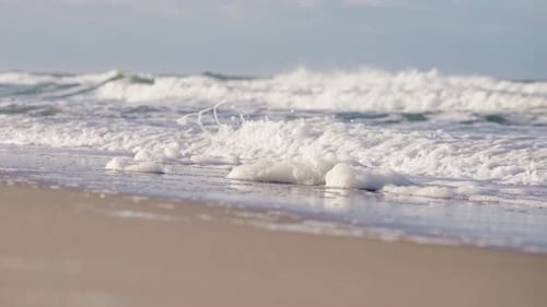 Breaking waves washing up white foam on sandy Sylt beach in Germany