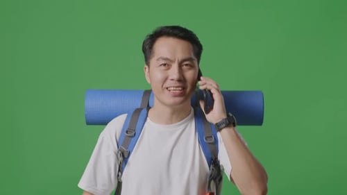 Close Up Of Asian Male Hiker Talking On Smartphone While Walking On Green Screen Background