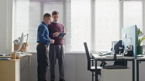 Two Male Colleagues Collaborating while Discussing Data in Notebook at Office