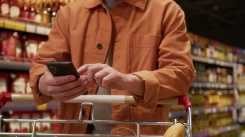 Midsection of Anonymous Man Using Phone and Leaning on Handle of Shopping Cart