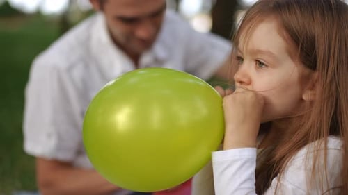 A Child Happily Blowing Up a Bright Green Balloon While Enjoying a Park Setting Outside