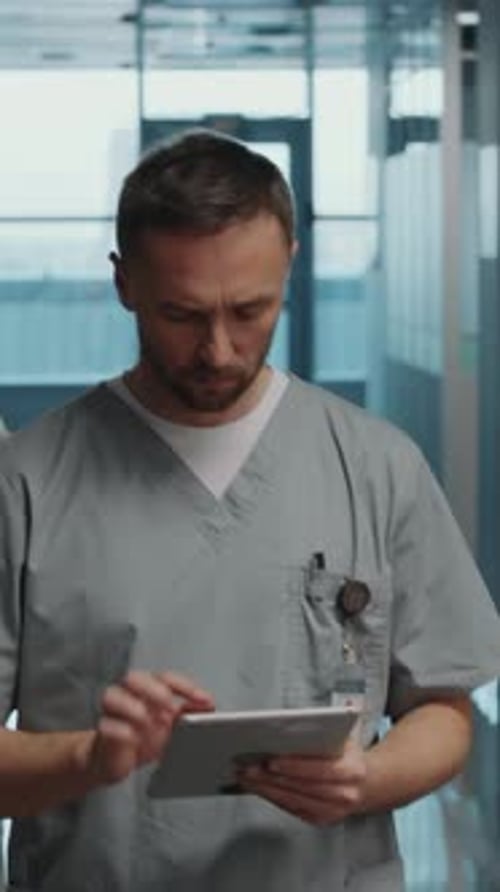 Doctor Walking through Hospital Corridor and Using Tablet