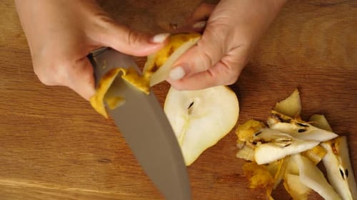 04 1Woman uses knife to cut out the core and seeds from half a pear on wooden board, with peels lyin