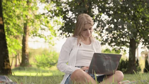 Woman Works on Laptop Sitting on Grass Outdoors