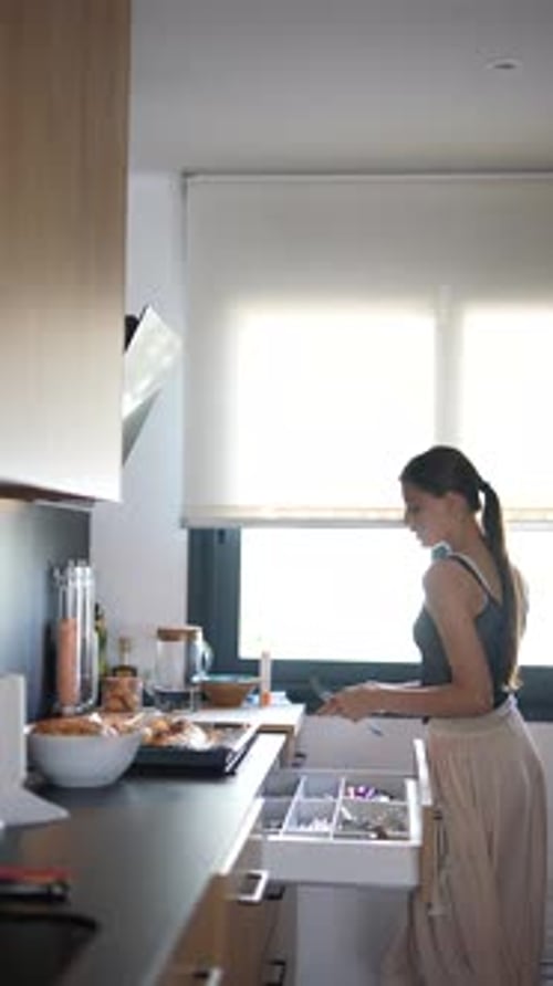 Une jeune femme range un tiroir de cuisine dans un cadre de cuisine moderne et lumineux