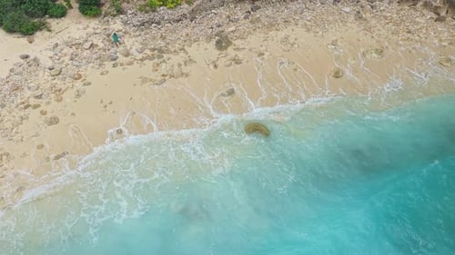Wunderschöne Luftaufnahme von oben nach unten auf türkisfarbene Meereswellen, die über einen abgelegenen Sandstrand an einem