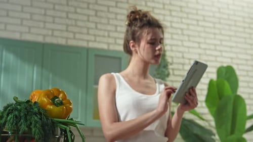 Young Woman at the Table in the Kitchen Preparing Spring Rolls for Healthy Lunch Reading Recipe on